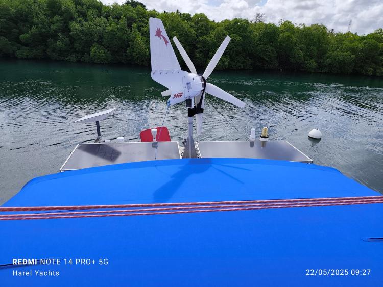 Custom Patago 40 boat with wind turbine, blue cover, and lush green background.