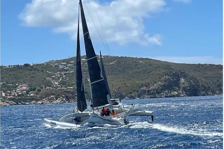 Sailing Coulombel Trimaran 1994 on blue ocean near rocky coastline under clear sky.