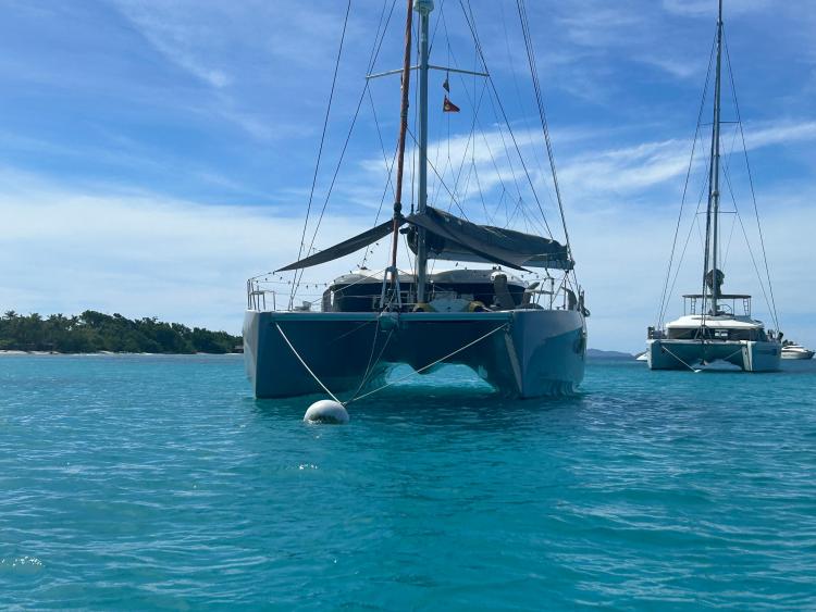 2024 Excess 14 catamaran anchored in clear turquoise waters, with a scenic island backdrop.
