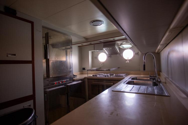 Galley kitchen inside a 1972 Benetti 33 yacht, featuring stainless steel appliances and porthole windows.