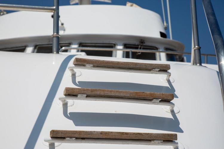 Close-up of wooden steps on a 1972 Benetti 33 yacht under clear blue sky.