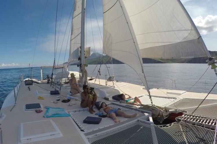 People relaxing on a 1995 Catamaran Day Charter Open Bridge Deck, sailing in clear waters.