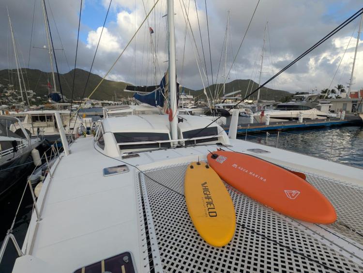 Catana 55 yacht with surfboards on deck, docked at marina, cloudy sky backdrop.